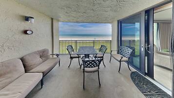 A balcony with a beige couch, a table with chairs, and a view of the beach.
