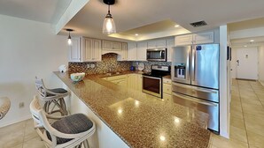 A modern kitchen with granite countertops, stainless steel appliances, and white cabinetry. - Sand Dollar II 207 by Distinctive Beach Rentals (St. Augustine)