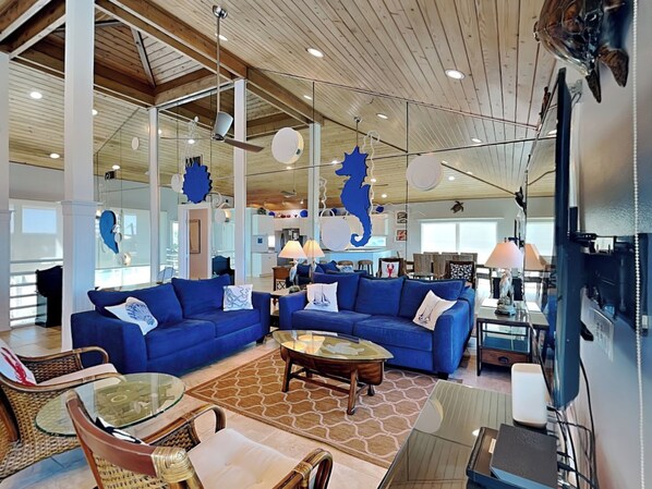 A spacious living area with two blue sofas, a glass coffee table, and a modern ceiling design. - Ocean Pearl by Distinctive Beach Rentals (St. Augustine)