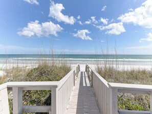 A wooden boardwalk leading to a beach with a clear sky and ocean view.