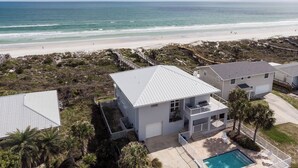En ejendom ved stranden med et stort hus, balkon, swimmingpool og udsigt over stranden.