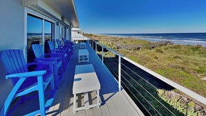 En balkon med blå stole og et lille bord, med udsigt over en strand og hav.