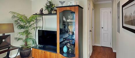 A living room with a wooden entertainment center, a flat-screen TV, a potted plant, and a dining area with a table and chairs.