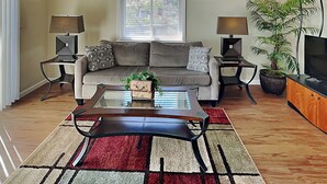 A living room with a sofa, two side tables with lamps, a coffee table, a TV, and a potted plant. - Sea Urchin 39 by Distinctive Beach Rentals (St. Augustine)
