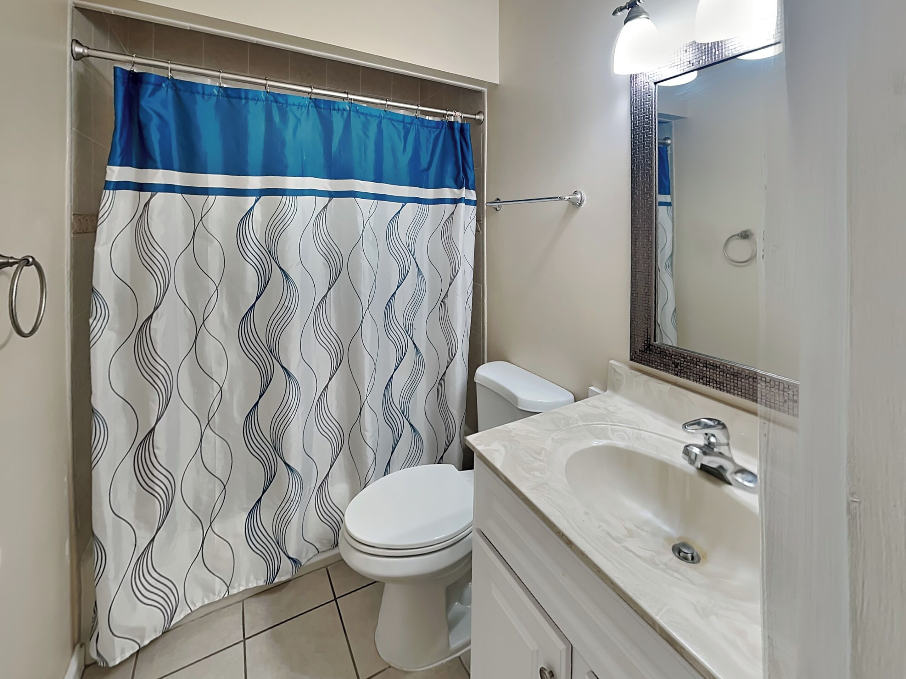 A bathroom with a shower curtain, toilet, sink, and mirror.