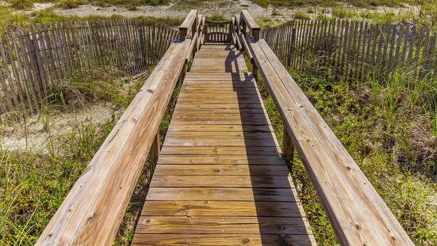 A wooden boardwalk leading to a beach with a wooden fence on either side. - Sea Urchin 39 by Distinctive Beach Rentals (St. Augustine)