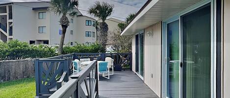 A wooden deck with outdoor seating, a glass door entrance, and a view of a residential building in the background.