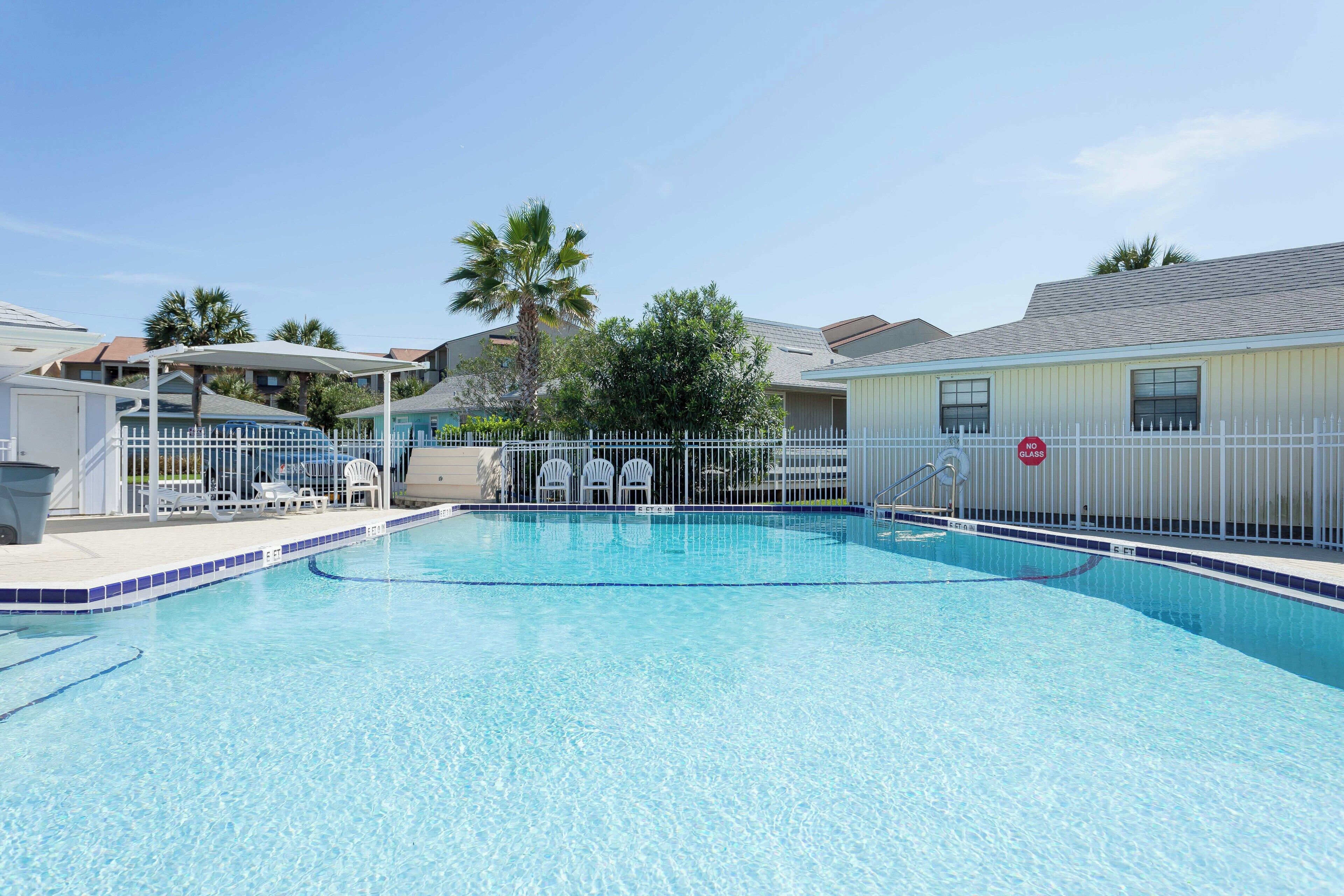 A clear swimming pool with a white fence, lounge chairs, and a no glass sign.
