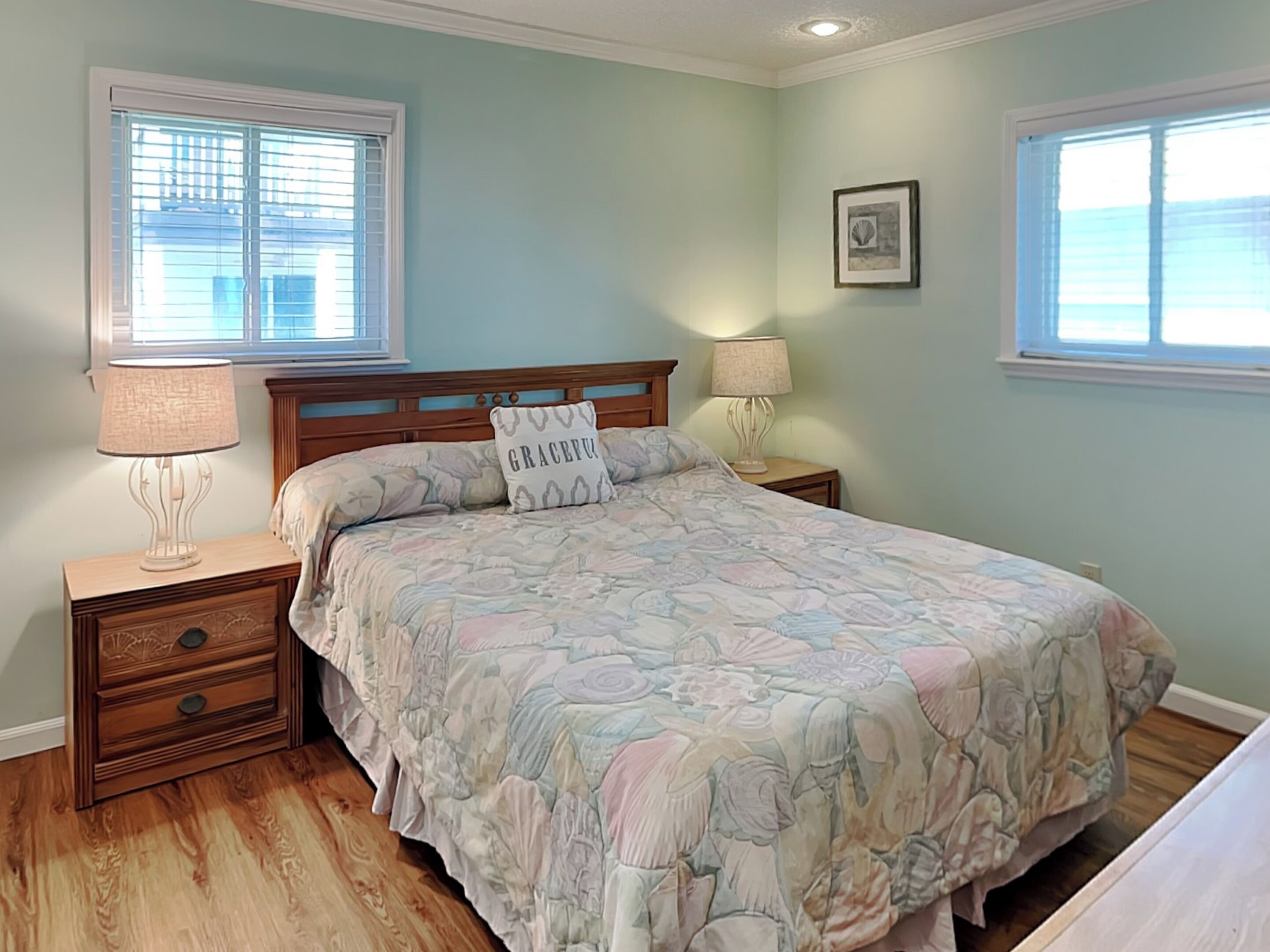 A bedroom with a bed, two bedside tables, a nightstand, a window, and a wall-mounted picture.