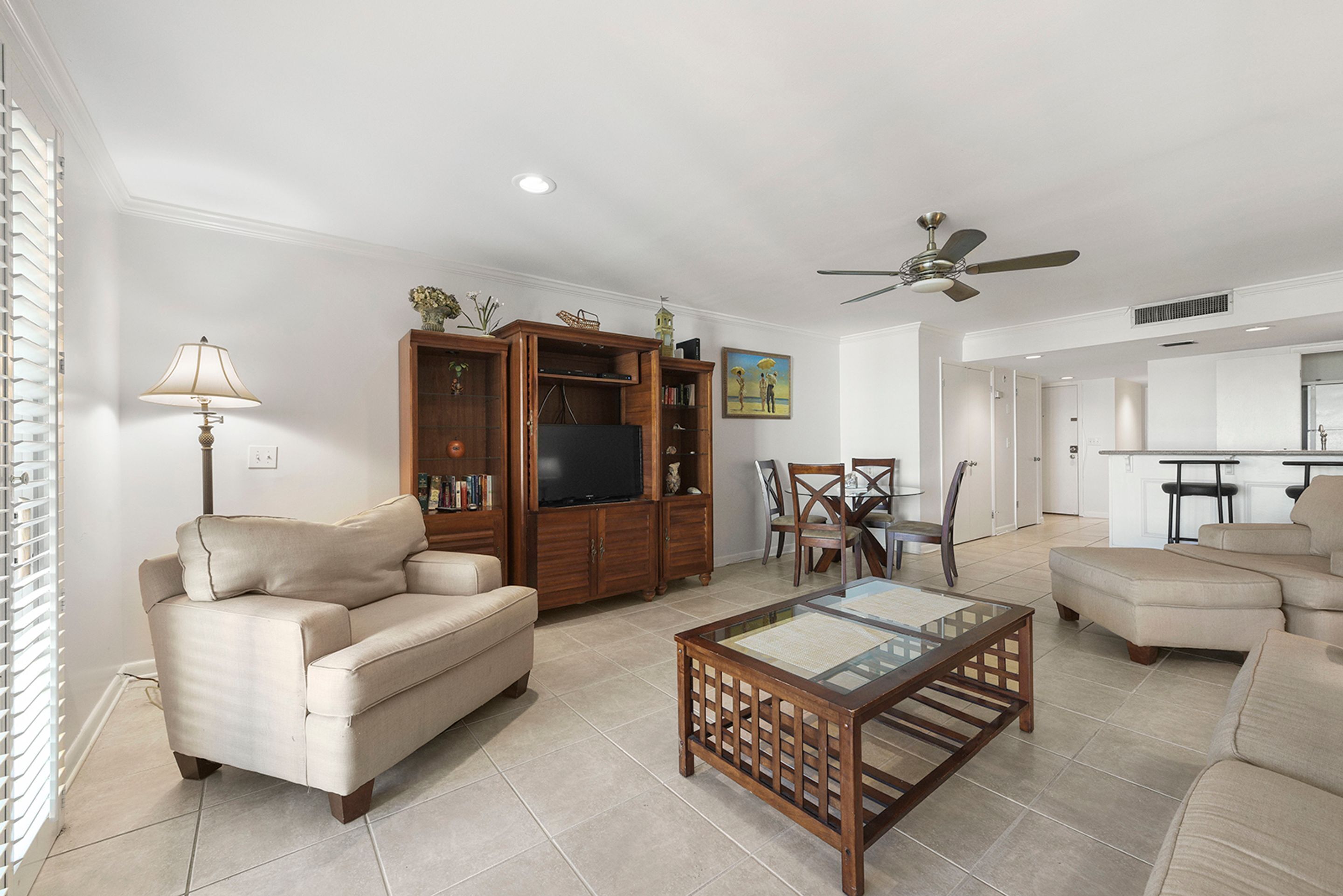 A living room with a beige sofa, a wooden entertainment unit, a glass coffee table, and a ceiling fan.
