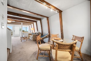 Enjoy a spacious room with a high ceiling, exposed beams, and a comfortable dining area with a glass table and cushioned chairs.