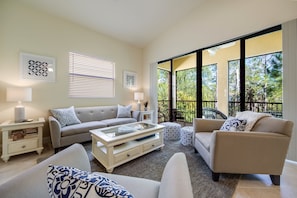 A modern living room with a beige sofa, a white coffee table, and patterned cushions. There are two side tables with lamps and a framed artwork on the wall. - Serrano 201 by Distinctive Beach Rentals (Bonita Springs)