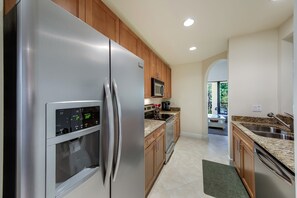 A modern kitchen with stainless steel appliances, wooden cabinets, and a granite countertop. - Serrano 201 by Distinctive Beach Rentals (Bonita Springs)