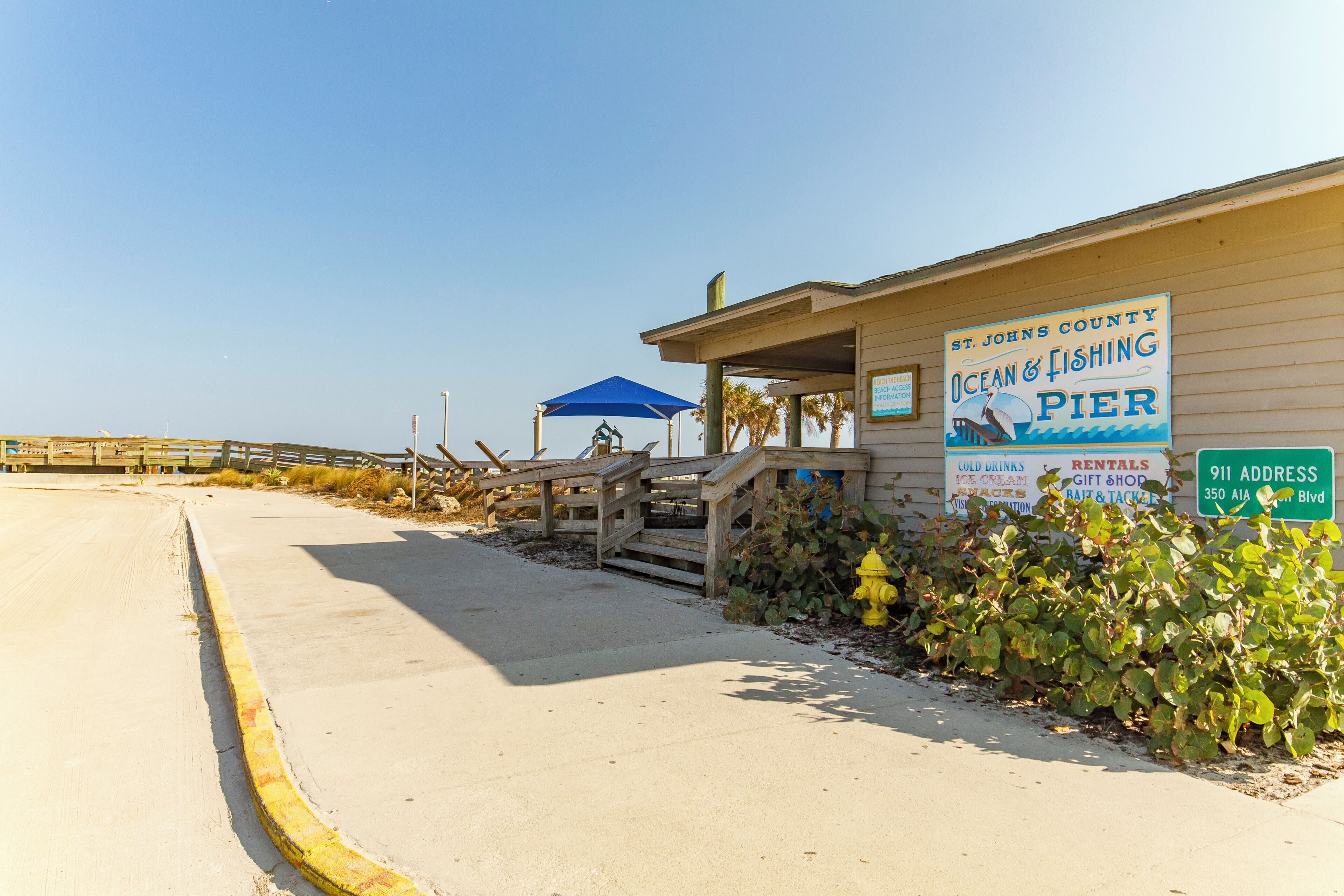 A pier with a sign for St. Johns County Ocean & Fishing Pier, including amenities like cold drinks, rentals, and a gift shop.