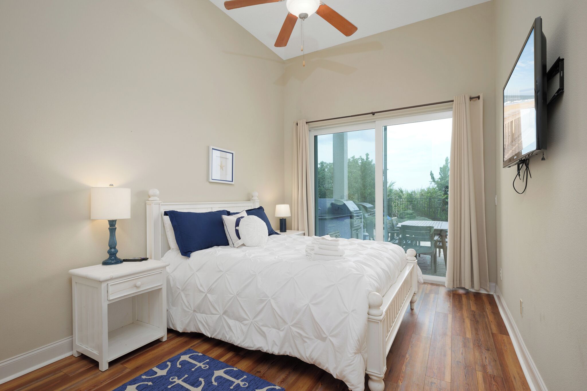 A bedroom with a bed, nightstands, a ceiling fan, a TV, and a large window with curtains.
