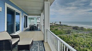 Een overdekt balkon met tuinmeubilair, een eethoek en uitzicht op de oceaan.