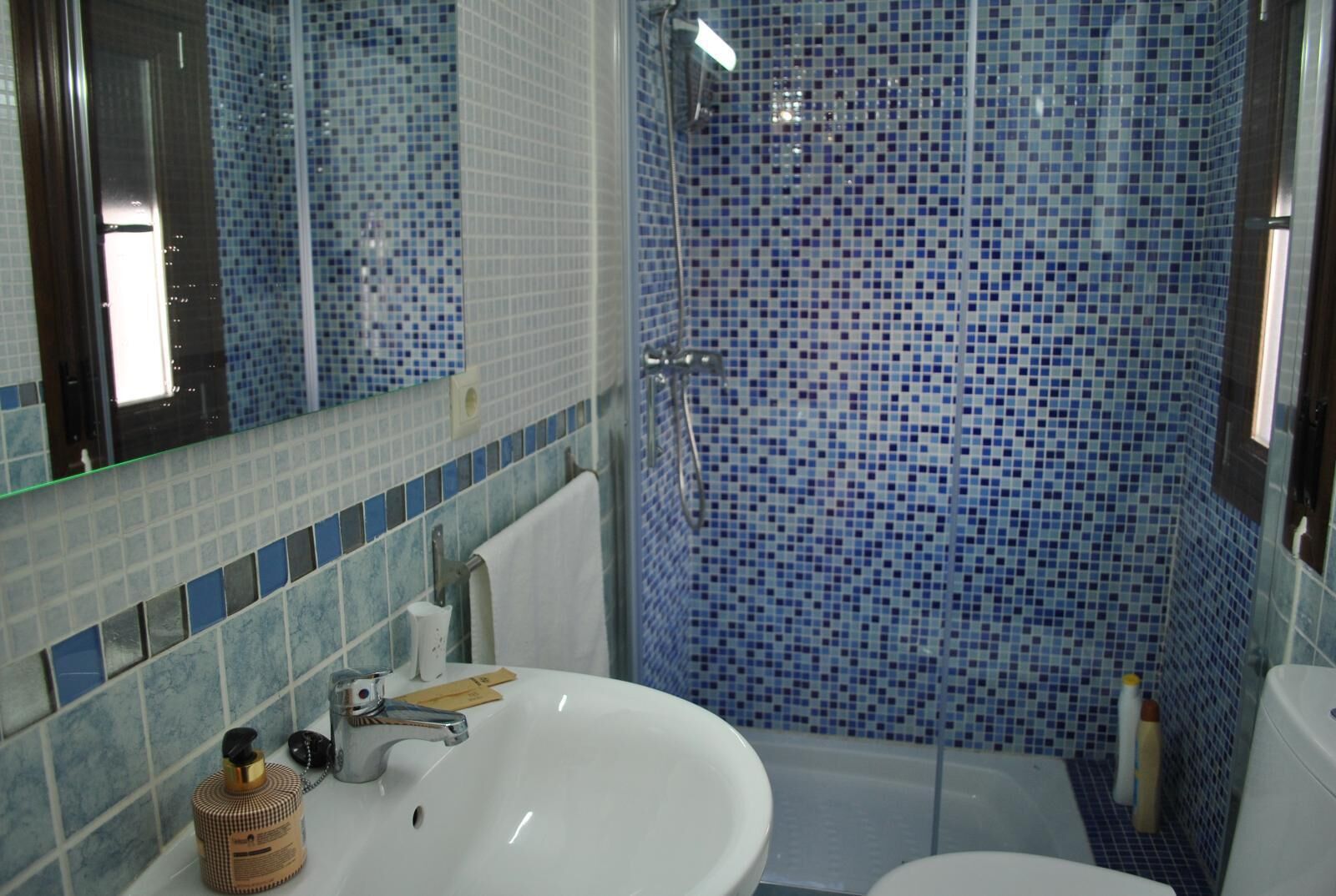 Une salle de bain avec un lavabo blanc, un miroir et une douche aux carreaux de mosaïque bleus.
