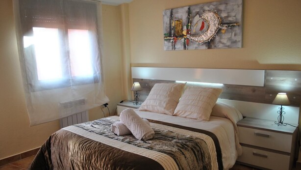 A bedroom with a bed, two bedside tables, a nightstand, a window with curtains, and a wall-mounted artwork. - Housing for tourist use Dulcinea (Duplex 4) Sales with Peña Aguilera (Las Ventas Con Peña Aguilera)