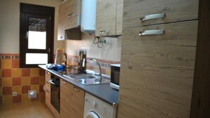 A compact kitchen with wooden cabinets, a built-in washing machine, and a tiled backsplash. - Housing for tourist use Dulcinea (Duplex 4) Sales with Peña Aguilera (Las Ventas Con Peña Aguilera)