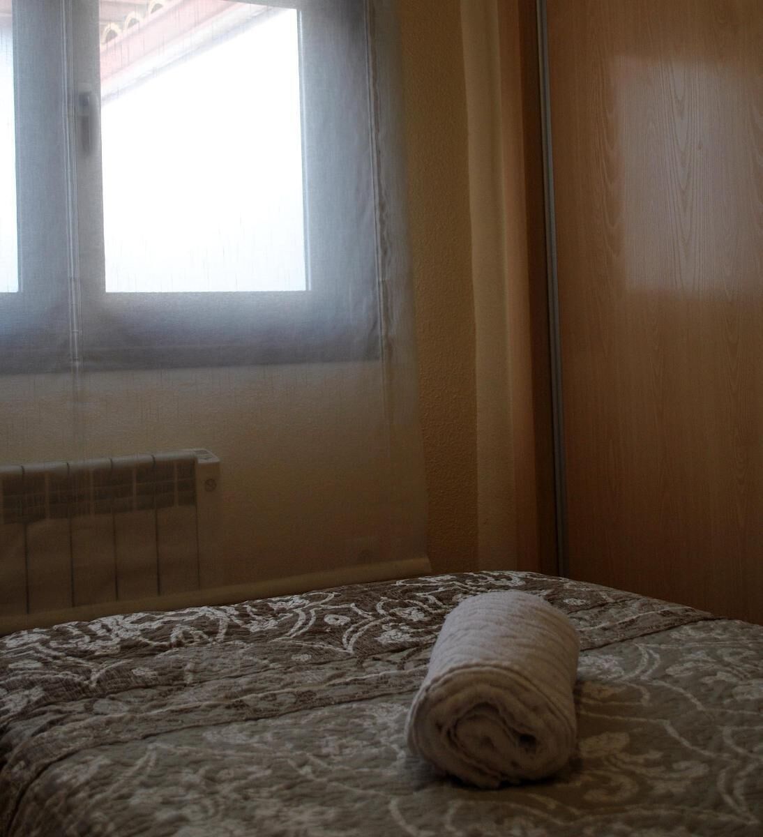 Una habitació amb un llit, una finestra amb cortines i un radiador.