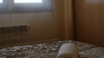 Una habitació amb un llit, una finestra amb cortines i un radiador.