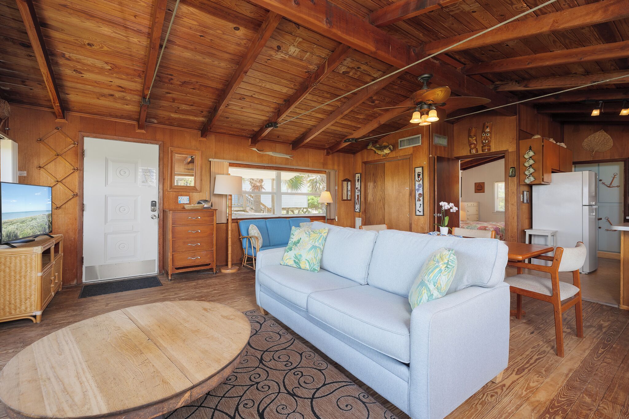 Ein gemütliches Blockhauskamin-Interieur mit einem hellblauen Sofa, Holzbalkendecke, Essbereich und einer Küche.