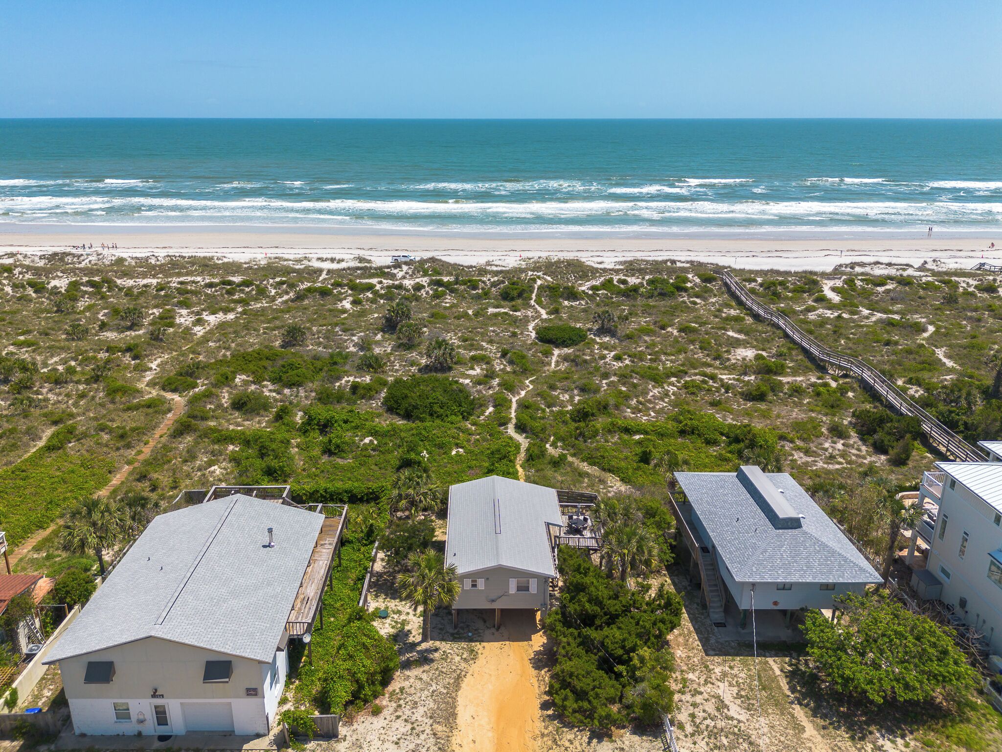 A coastal area with a beach, a wooden boardwalk, and several buildings with flat roofs.