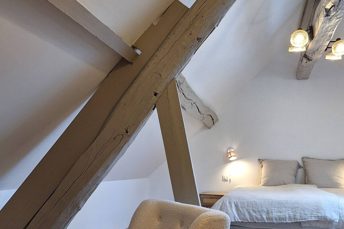 Une chambre mansardée avec des poutres apparentes, un lit, une table de chevet et une chaise.