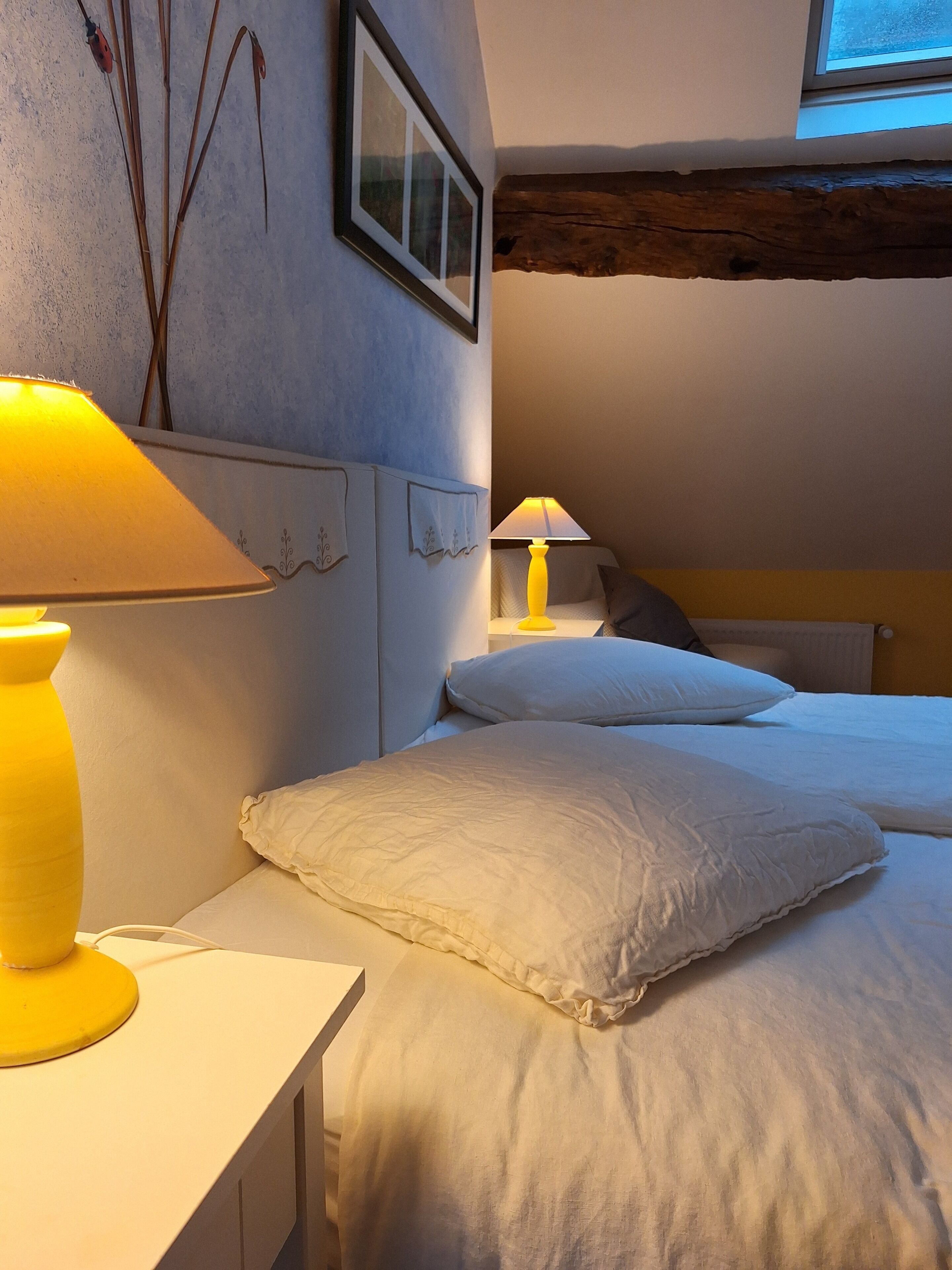 A bedroom with a bed, bedside lamps, a framed picture, and a window.