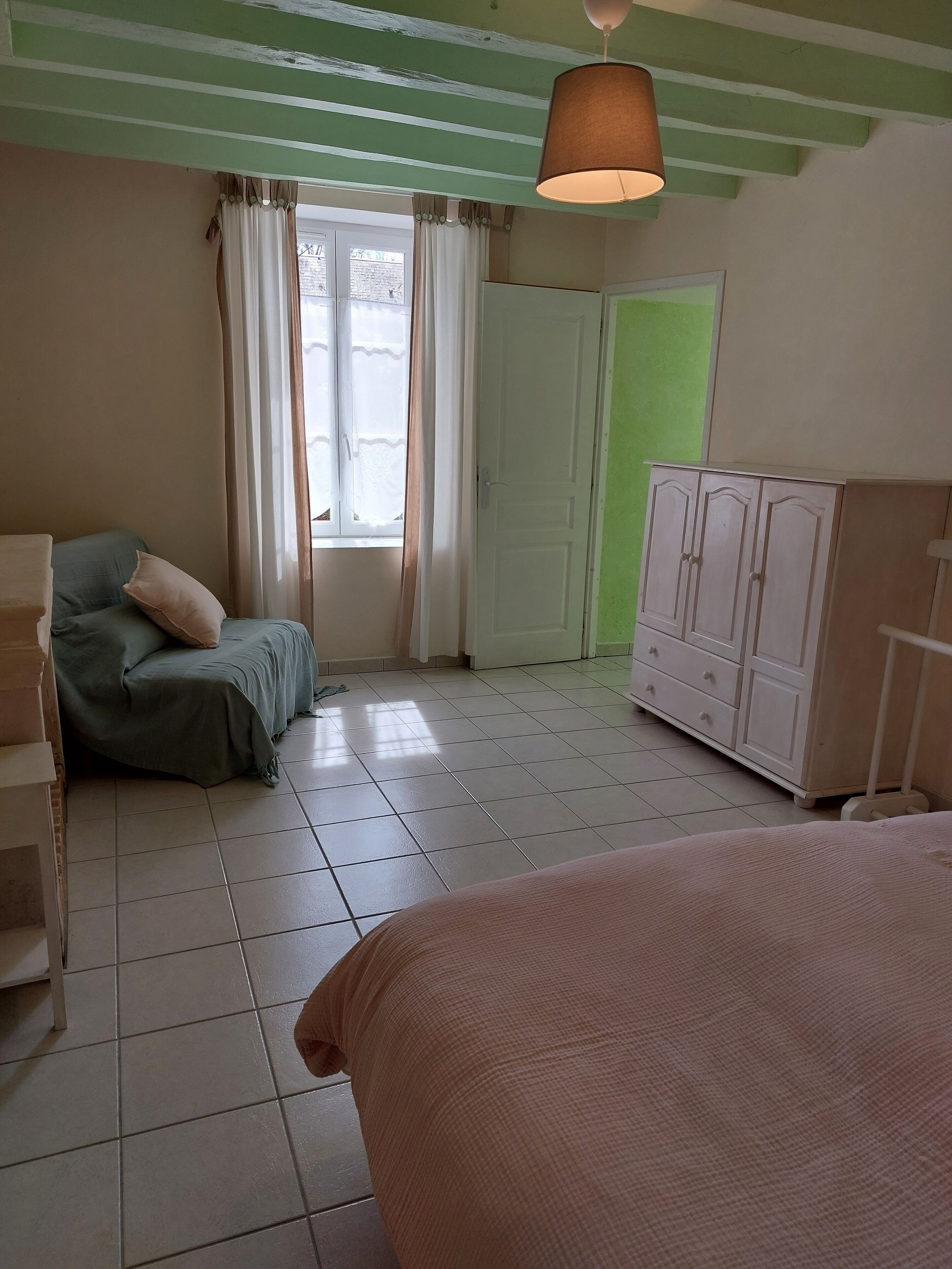 Ein Schlafzimmer mit Bett, Stuhl, Kleiderschrank und einem Fenster mit Vorhängen.