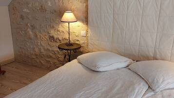 A bedroom with a sloped ceiling, a bed with white bedding, a bedside lamp, and a brick wall.