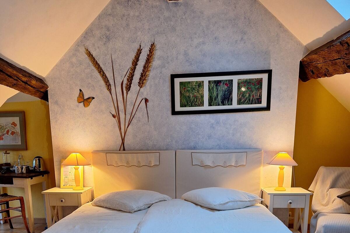 Une chambre confortable avec un grand lit, deux tables de chevet avec des lampes, un tableau encadré au mur et une poutre en bois au plafond.