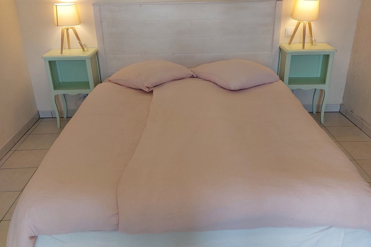 Un lit avec une tête de lit blanche, deux tables de chevet avec des lampes et une couverture beige.