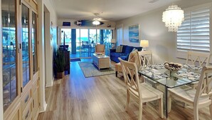 A spacious living area with a glass dining table, a blue sofa, and a ceiling fan.