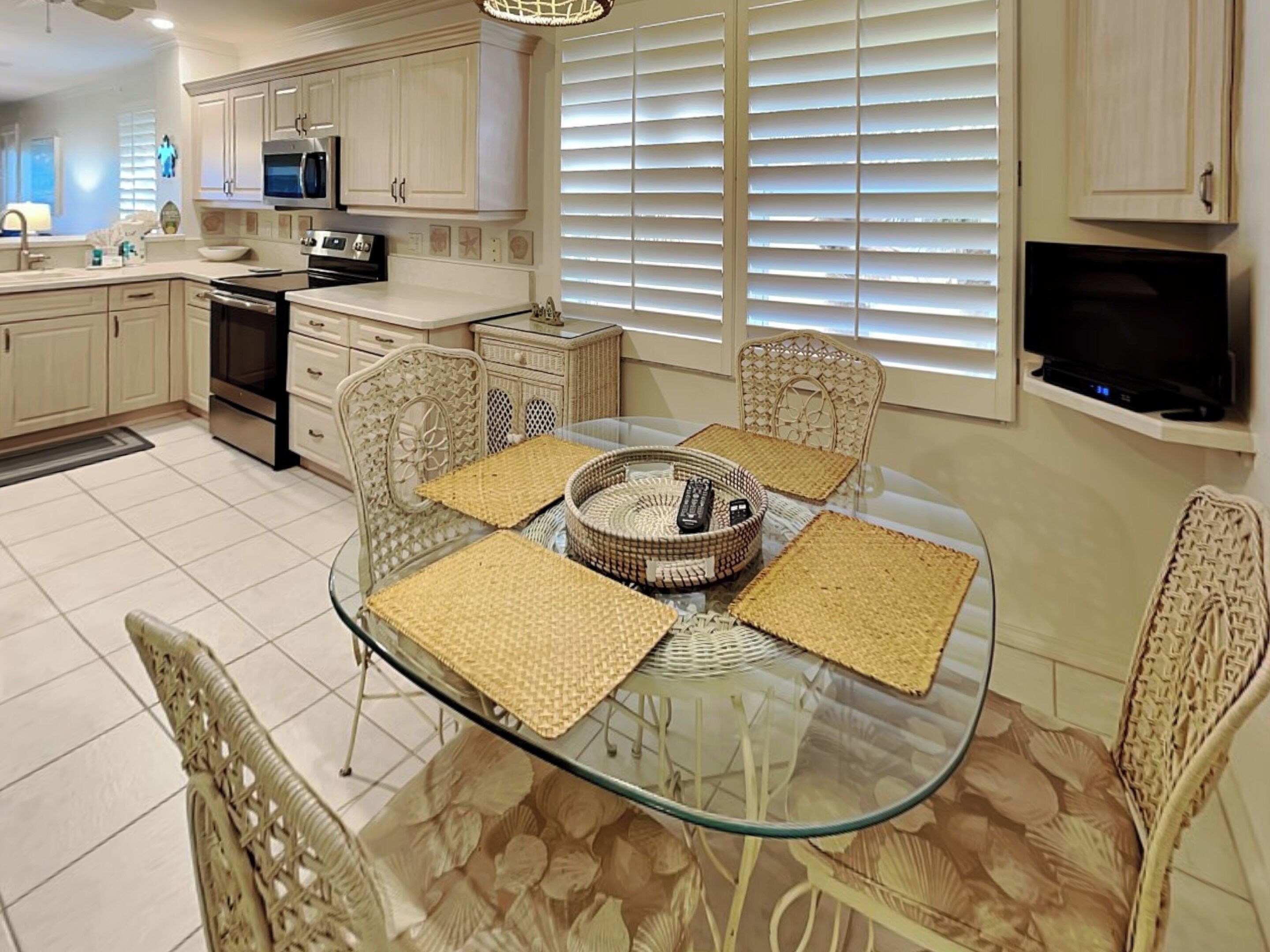 A modern kitchen with white cabinets, a microwave, and a stove. There is a glass dining table with four chairs and a woven basket.