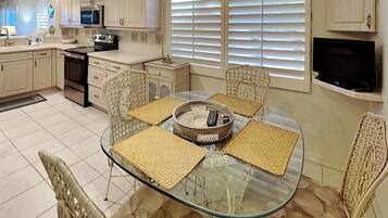 A modern kitchen with white cabinets, a microwave, and a stove. There is a glass dining table with four chairs and a woven basket.