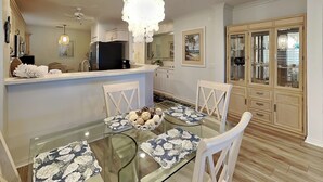 A dining area with a glass table, white chairs, and a chandelier.