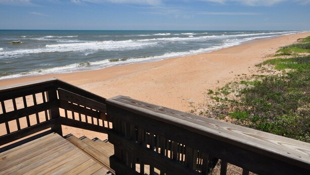A wooden deck overlooking a sandy beach with waves.