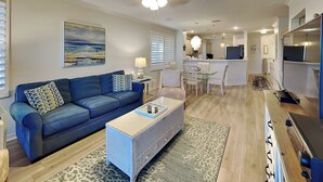 A modern living room with a blue sofa, a coffee table, and a dining area with a chandelier.