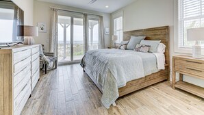 A bedroom with a large bed, a ceiling fan, a dresser, a nightstand, and a view through a glass door.