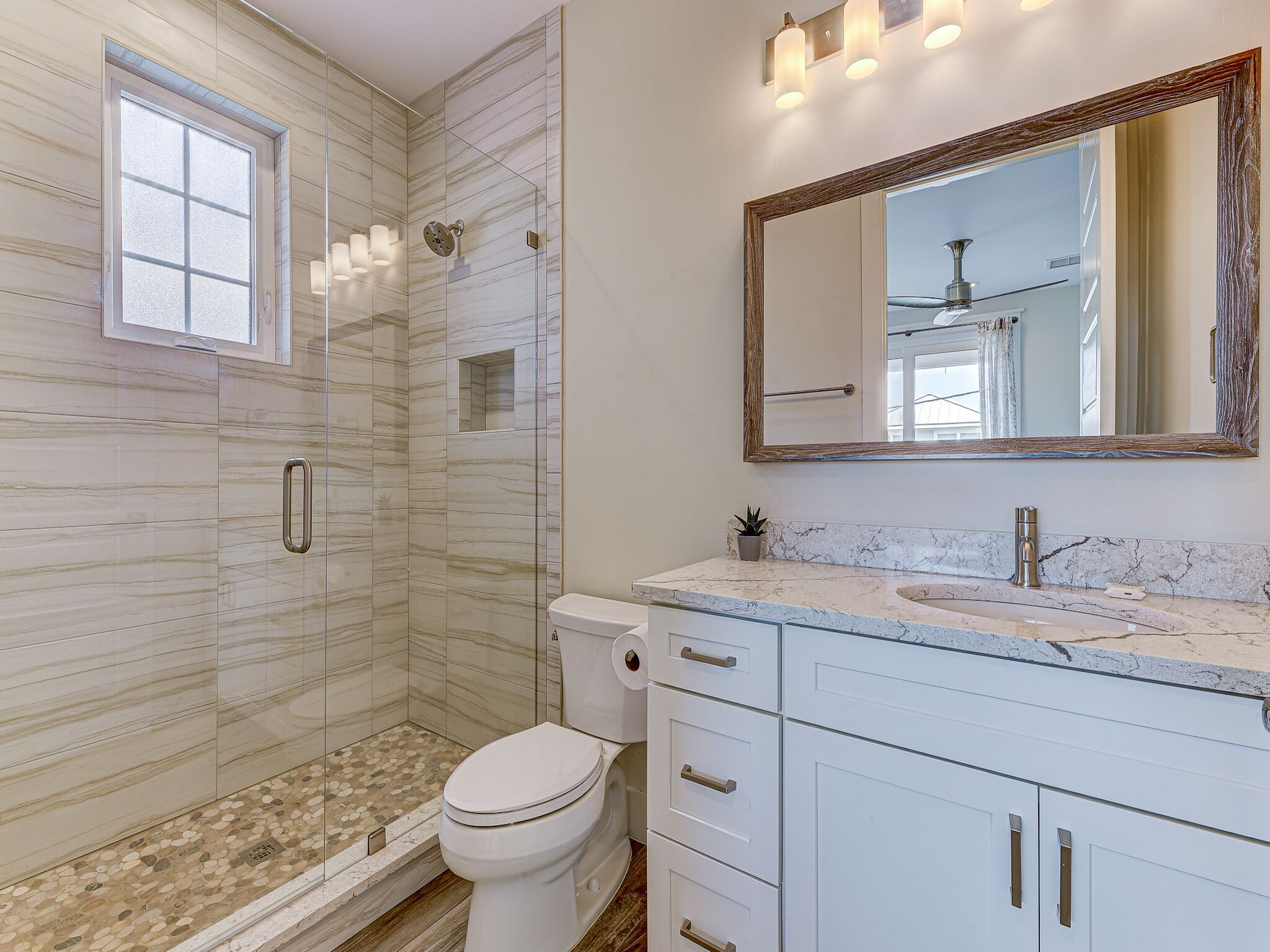 A modern bathroom with a glass-enclosed shower, a white toilet, a marble sink, and a large mirror.
