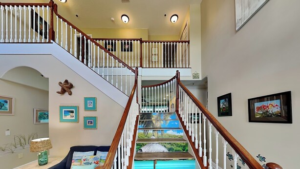 A staircase with a wooden handrail and white balusters, leading to an upper level. - Seas the Day by Distinctive Beach Rentals (Flagler Beach)