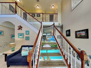 A staircase with a wooden handrail and white balusters, leading to an upper level. - Seas the Day by Distinctive Beach Rentals (Flagler Beach)
