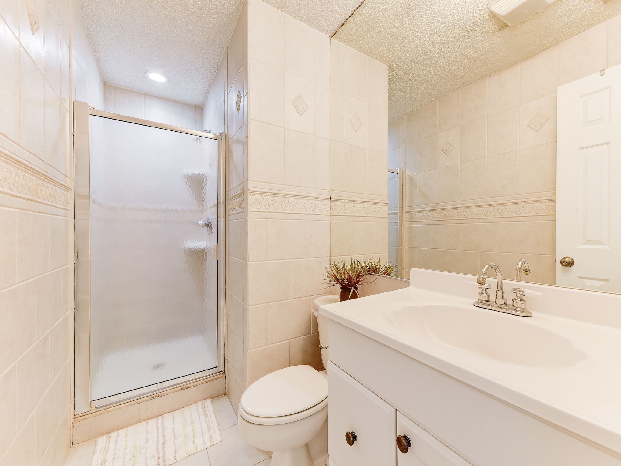 A bathroom with a glass shower enclosure, a white toilet, and a vanity with a sink and mirror.