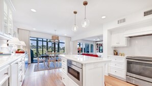 A modern kitchen with white cabinetry, a central island, stainless steel appliances, and a view to the outdoors. - Ponte Vedra Deer Run 9770 by Distinctive Beach Rentals (Ponte Vedra Beach)