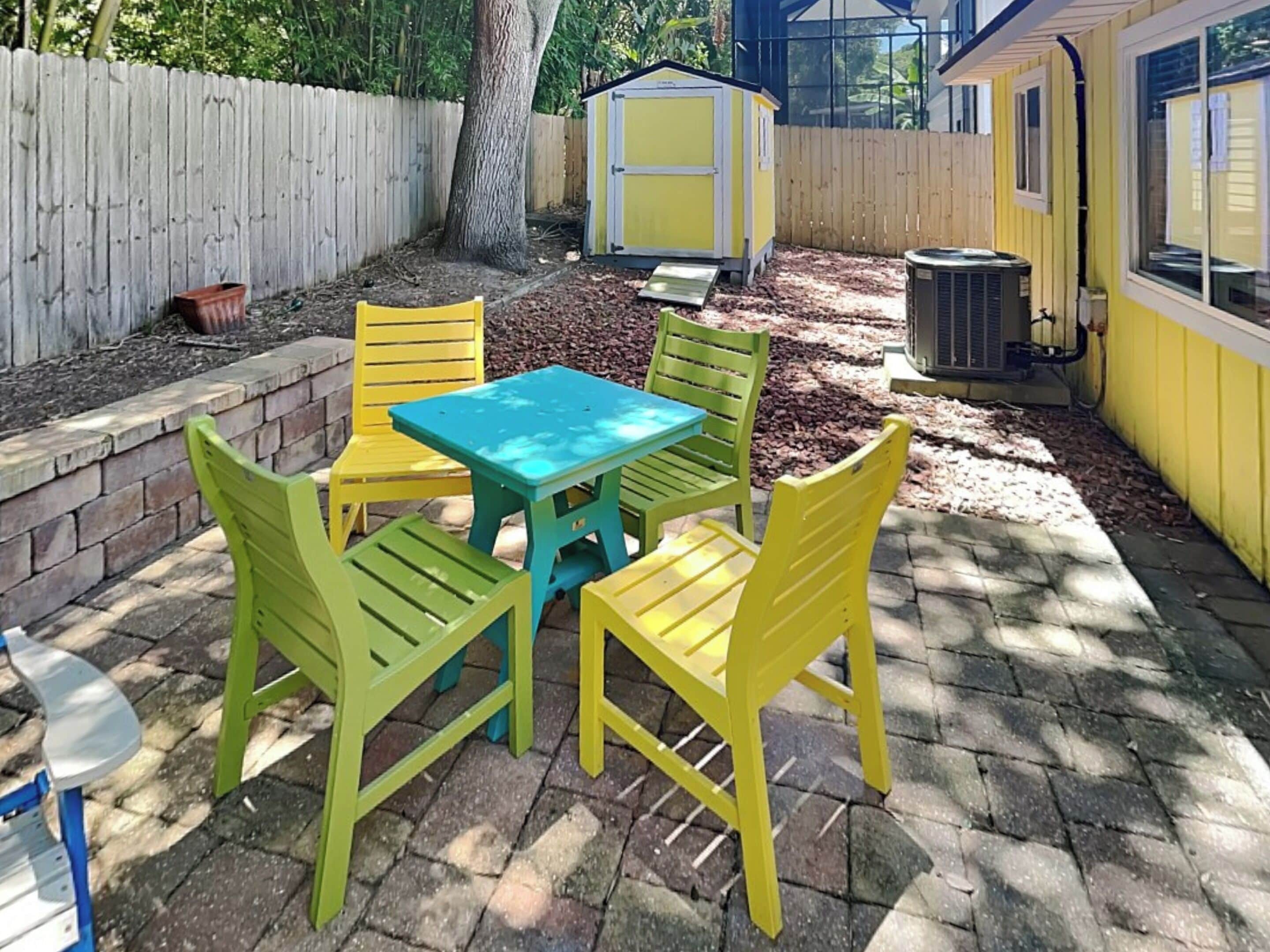 A patio with a table and chairs, surrounded by a wooden fence and a shed.
