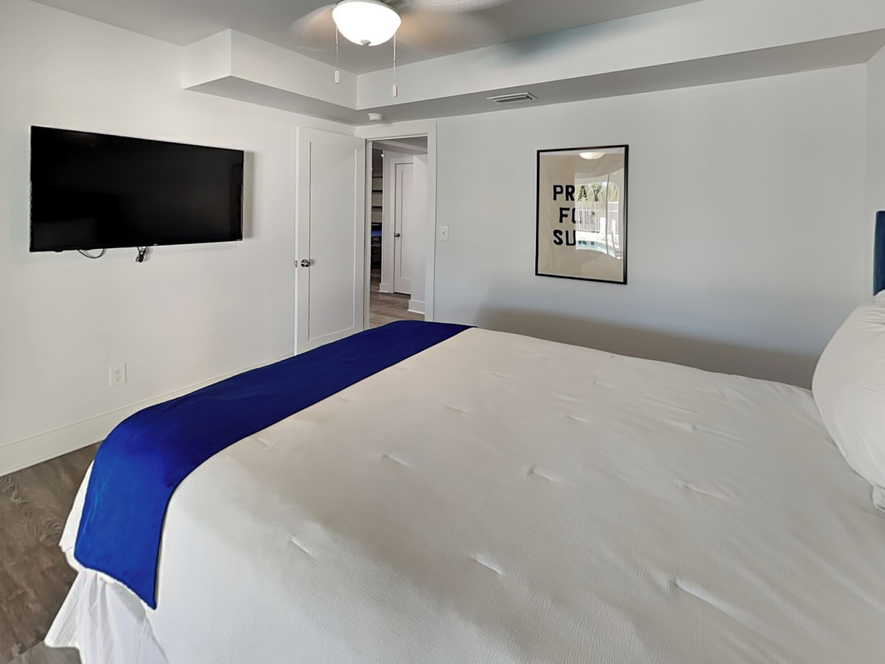 Un dormitorio con una cama, un televisor de pantalla plana montado en la pared y un cartel enmarcado en la pared.