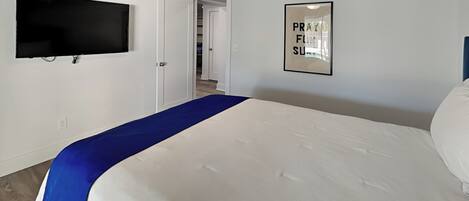 Un dormitorio con una cama, un televisor de pantalla plana montado en la pared y un cartel enmarcado en la pared.