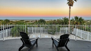 Eine Terrasse mit zwei Stühlen, die auf ein weißes Zaunfeld mit Blick auf einen Strand bei Sonnenuntergang zeigen.
