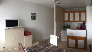 Een kleine keuken met houten kastjes, een koelkast, een magnetron en een televisie op een kastje.